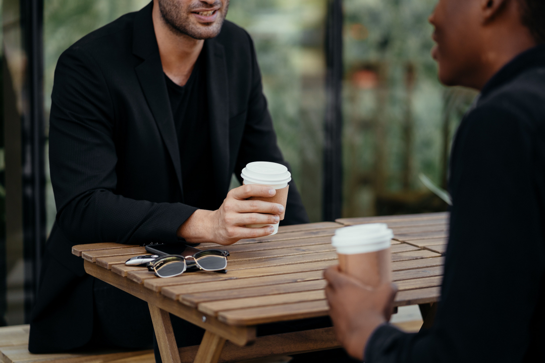 Two adults enjoying a coffee meeting outdoors, holding disposable cups on a wooden table