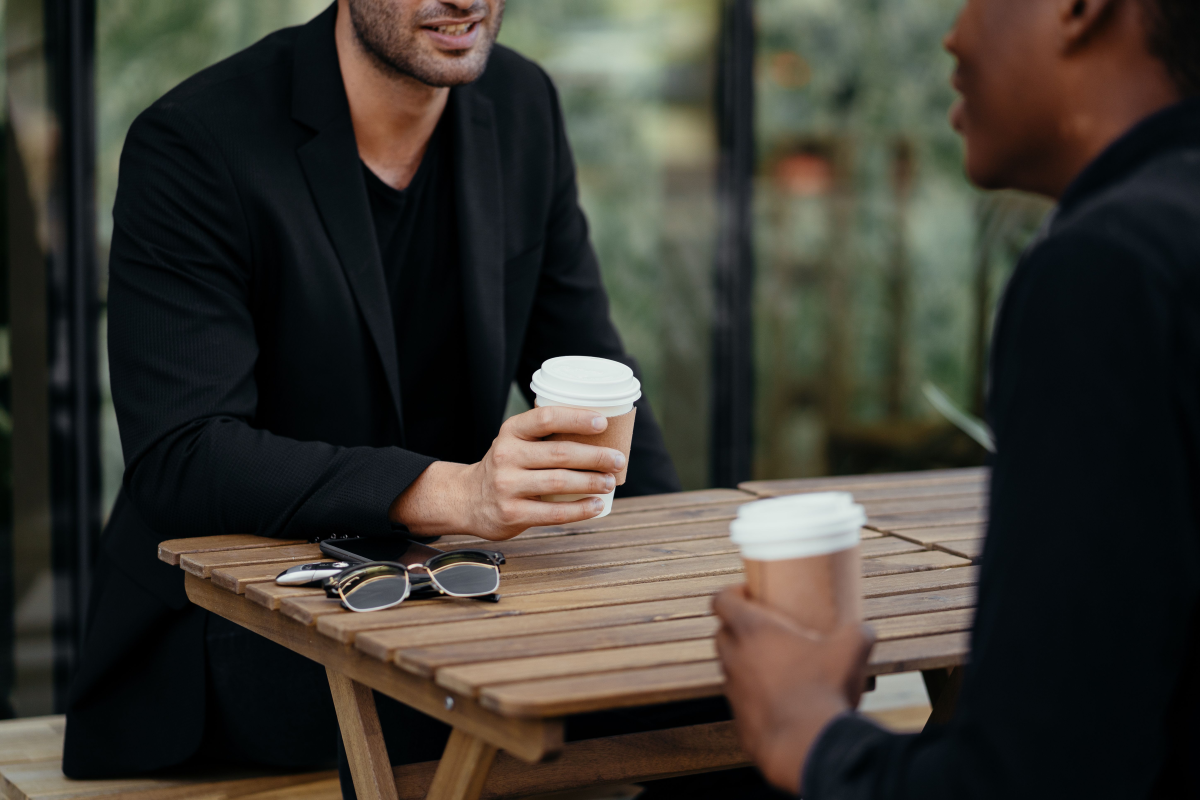 Two adults enjoying a coffee meeting outdoors, holding disposable cups on a wooden table